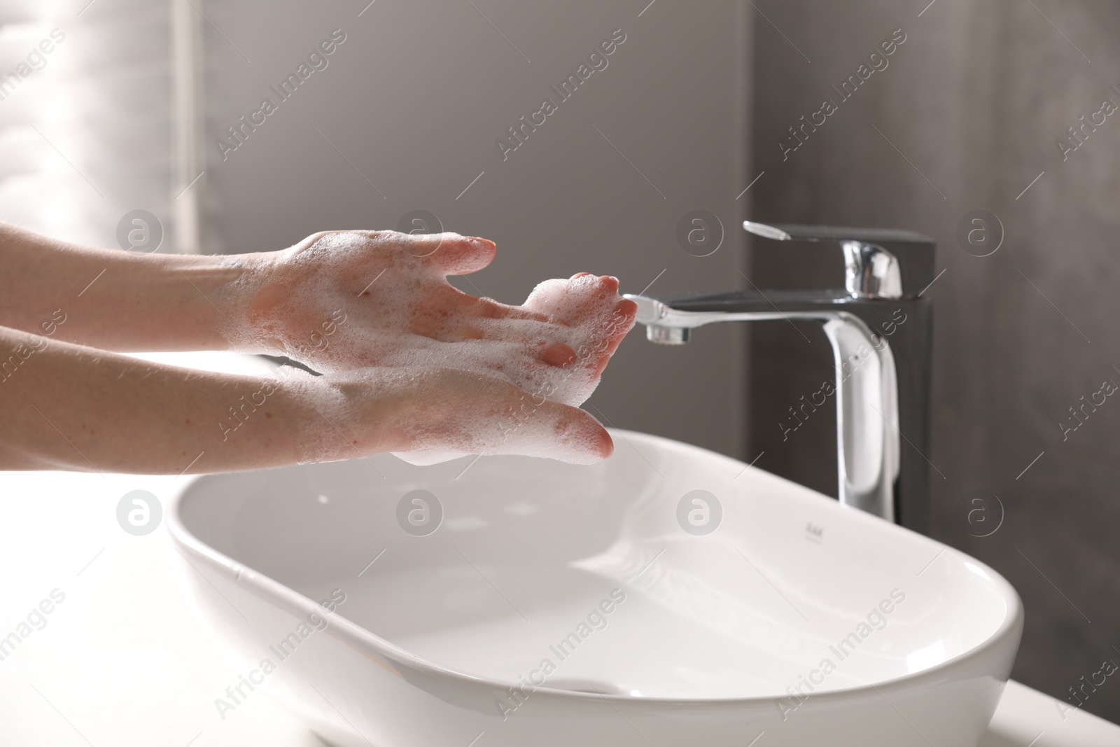 Photo of Woman washing hands with cleansing foam near sink in bathroom, closeup