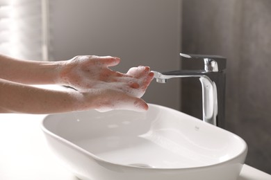 Woman washing hands with cleansing foam near sink in bathroom, closeup
