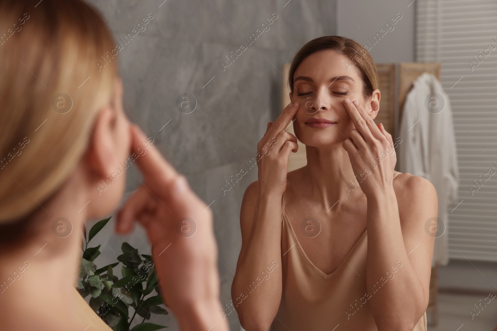 Photo of Woman massaging her face near mirror in bathroom