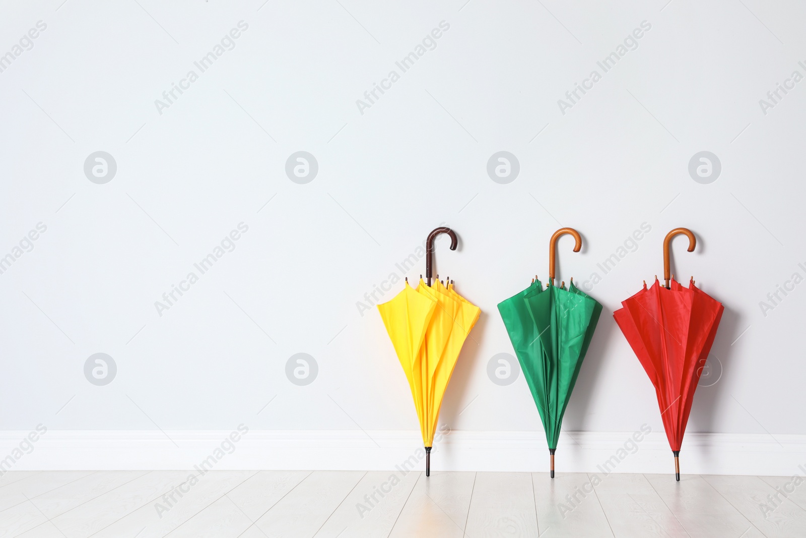 Photo of Beautiful bright umbrellas on floor near white wall with space for design