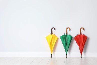 Photo of Beautiful bright umbrellas on floor near white wall with space for design