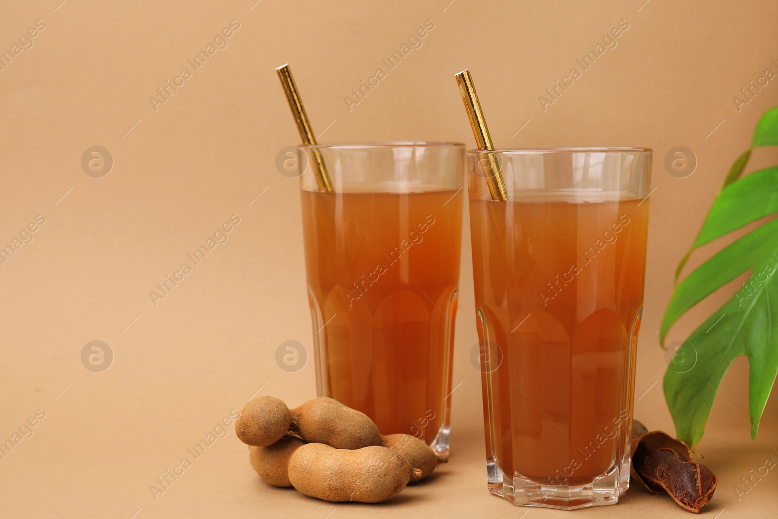 Photo of Tamarind juice, fresh fruits and green leaf on pale brown background, space for text