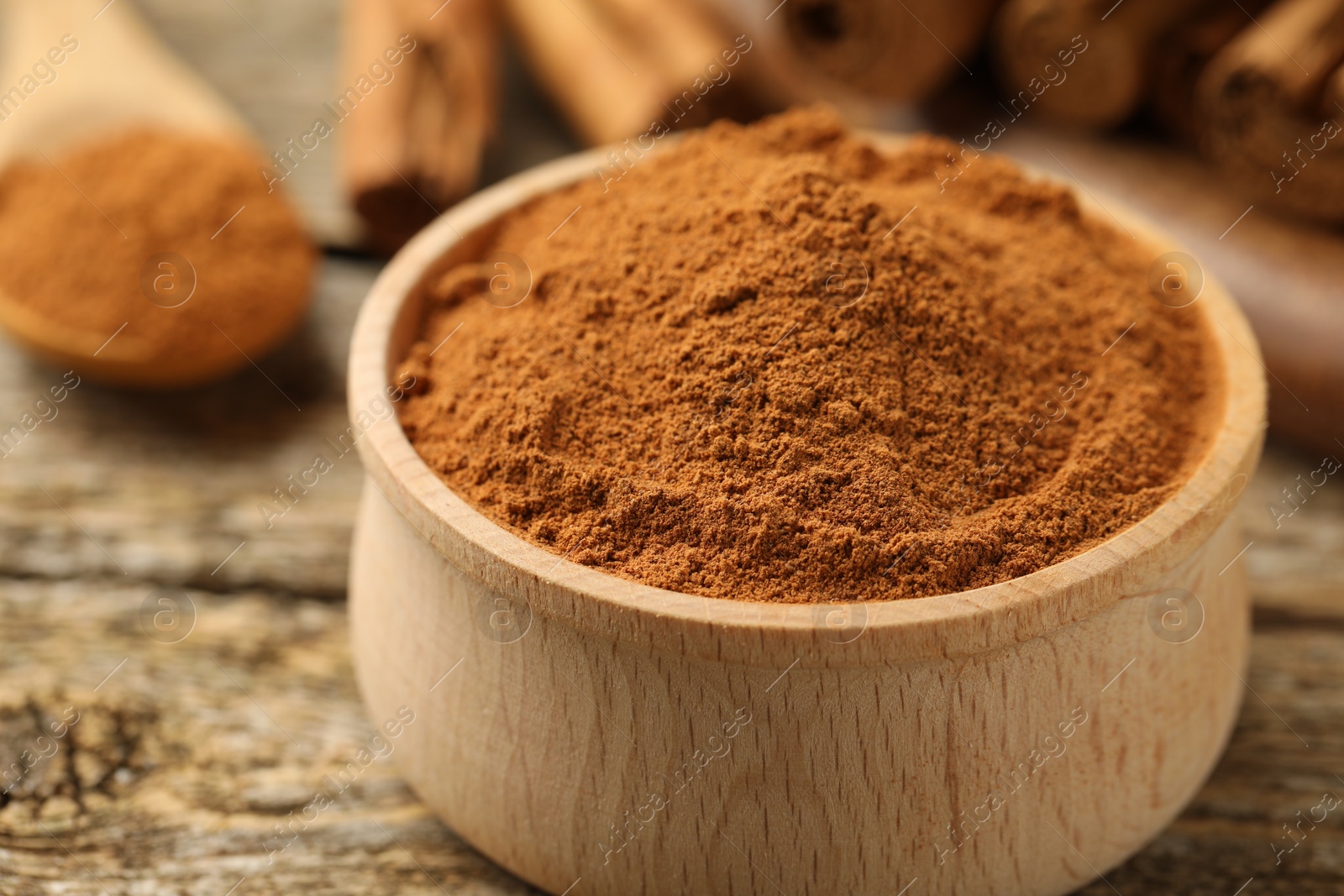 Photo of Bowl of cinnamon powder on wooden table, closeup