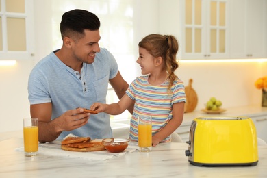 Photo of Father and daughter having breakfast with toasted bread at table in kitchen