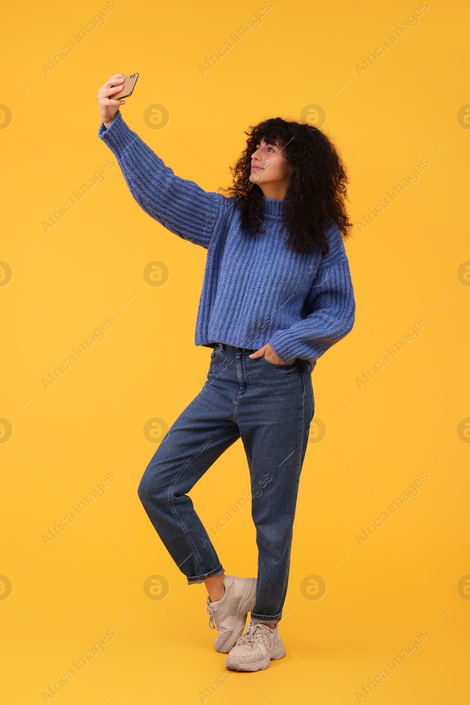 Photo of Beautiful young woman taking selfie with smartphone on orange background