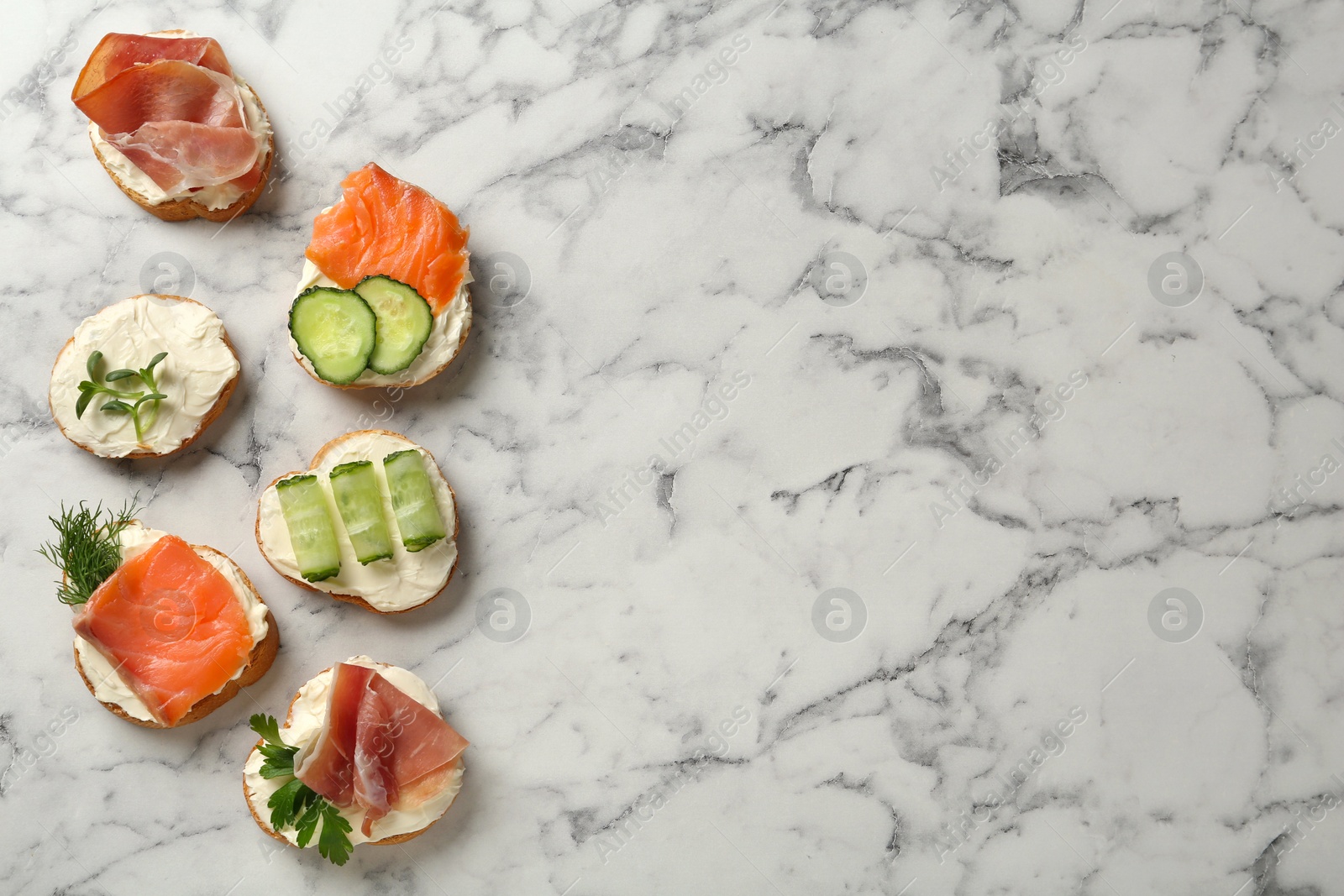 Photo of Delicious sandwiches with cream cheese and other ingredients on white marble table, flat lay. Space for text