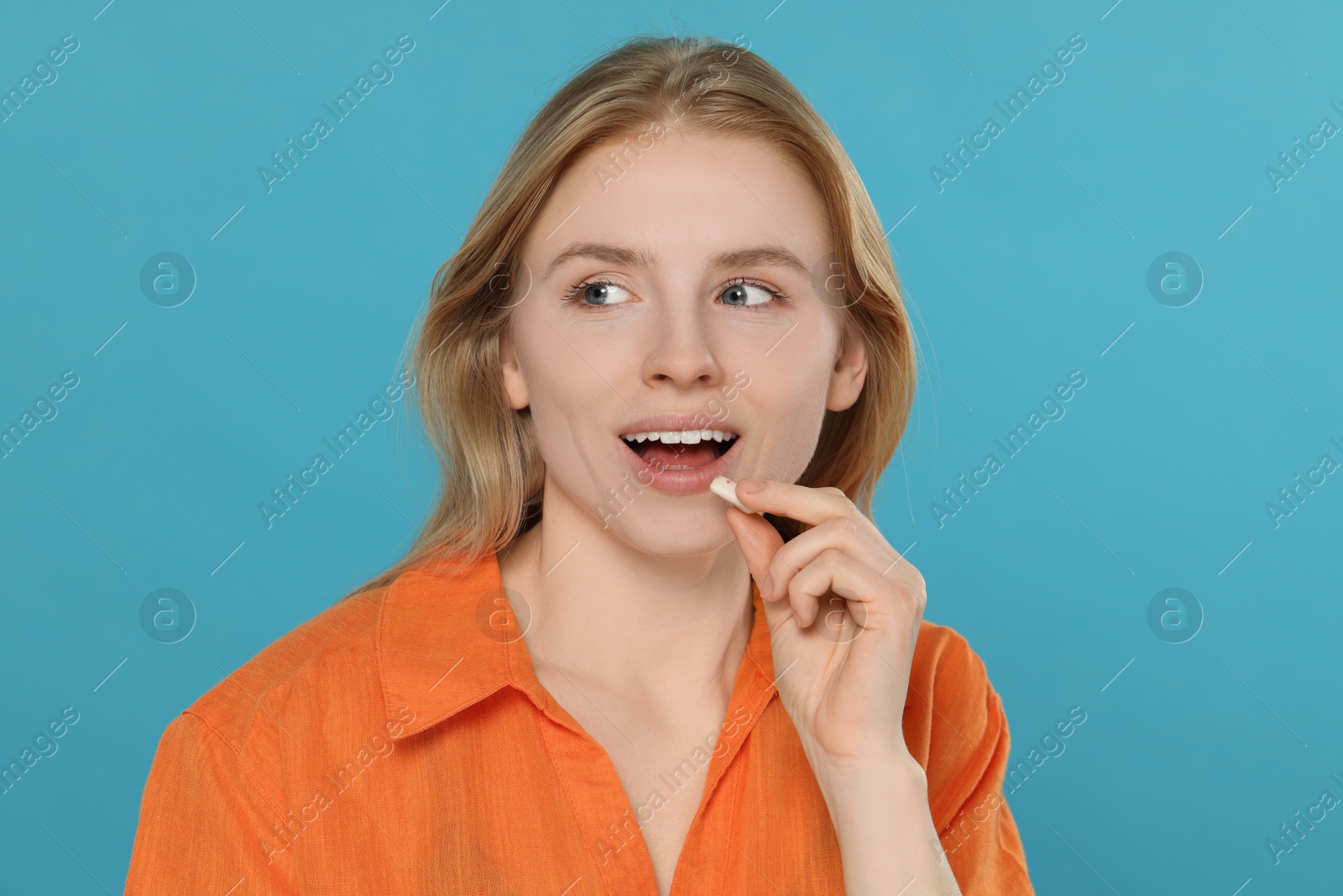 Photo of Happy young woman putting bubble gum into mouth on light blue background