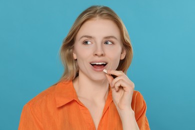 Happy young woman putting bubble gum into mouth on light blue background