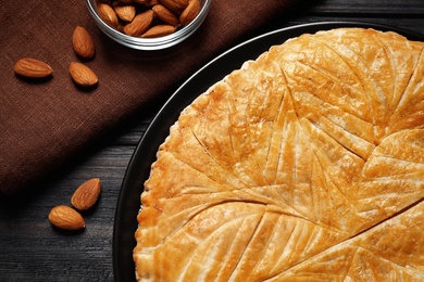 Photo of Traditional galette des rois and almonds on black wooden table, flat lay