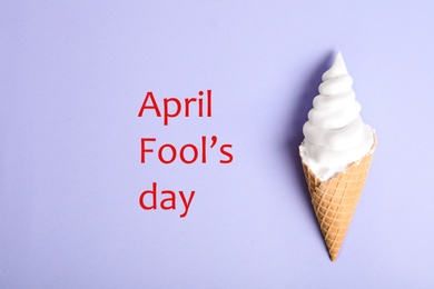 Top view of ice cream cone with shaving foam on violet background, space for text. April Fool's Day