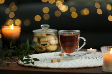 Tea, cookies and decorative elements on wooden table against blurred lights indoors