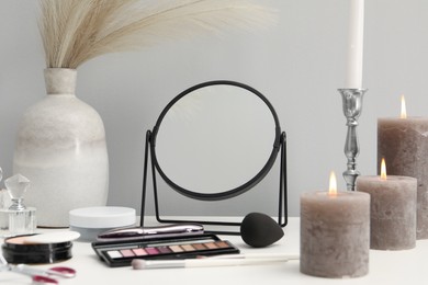 Dressing table with mirror, cosmetic products and burning candles in makeup room