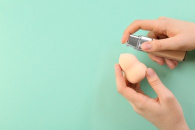 Photo of Woman adding skin foundation onto makeup sponge on mint color background, top view. Space for text
