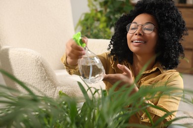Happy woman spraying beautiful houseplant leaves with water indoors