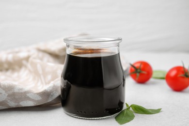 Photo of Glass jar with balsamic vinegar, basil and tomatoes on white table