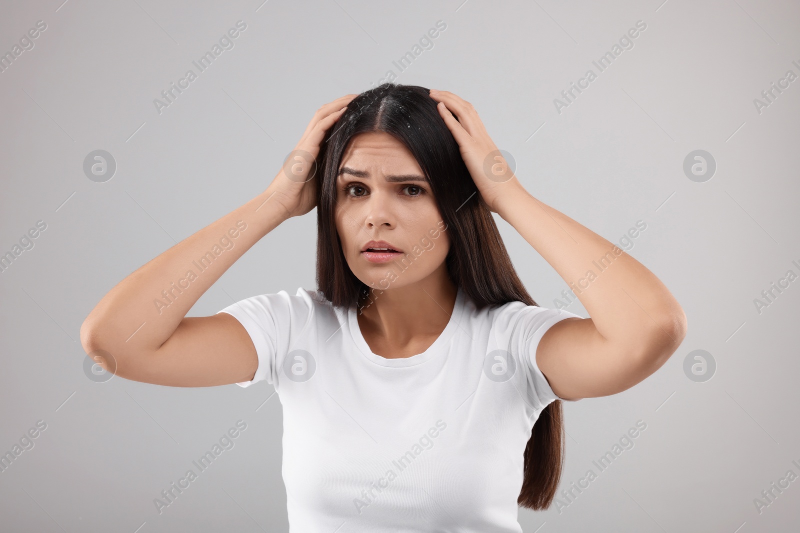 Photo of Emotional woman examining her hair and scalp on grey background. Dandruff problem