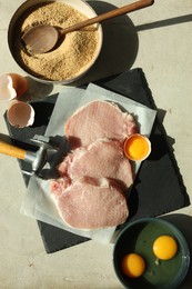 Photo of Cooking schnitzel. Raw pork chops, meat mallet and ingredients on grey table, flat lay