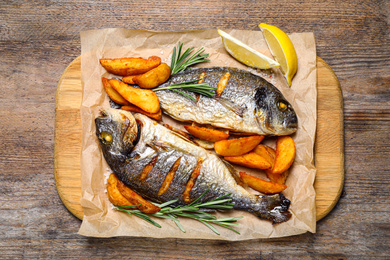 Delicious roasted fish and potatoes on wooden table, flat lay