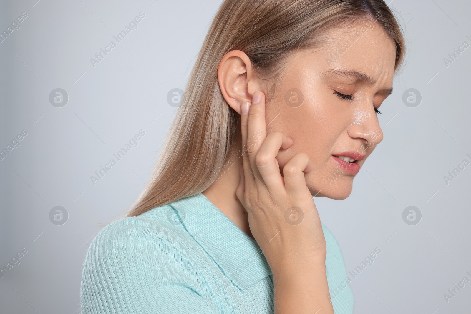 Photo of Young woman suffering from ear pain on light grey background