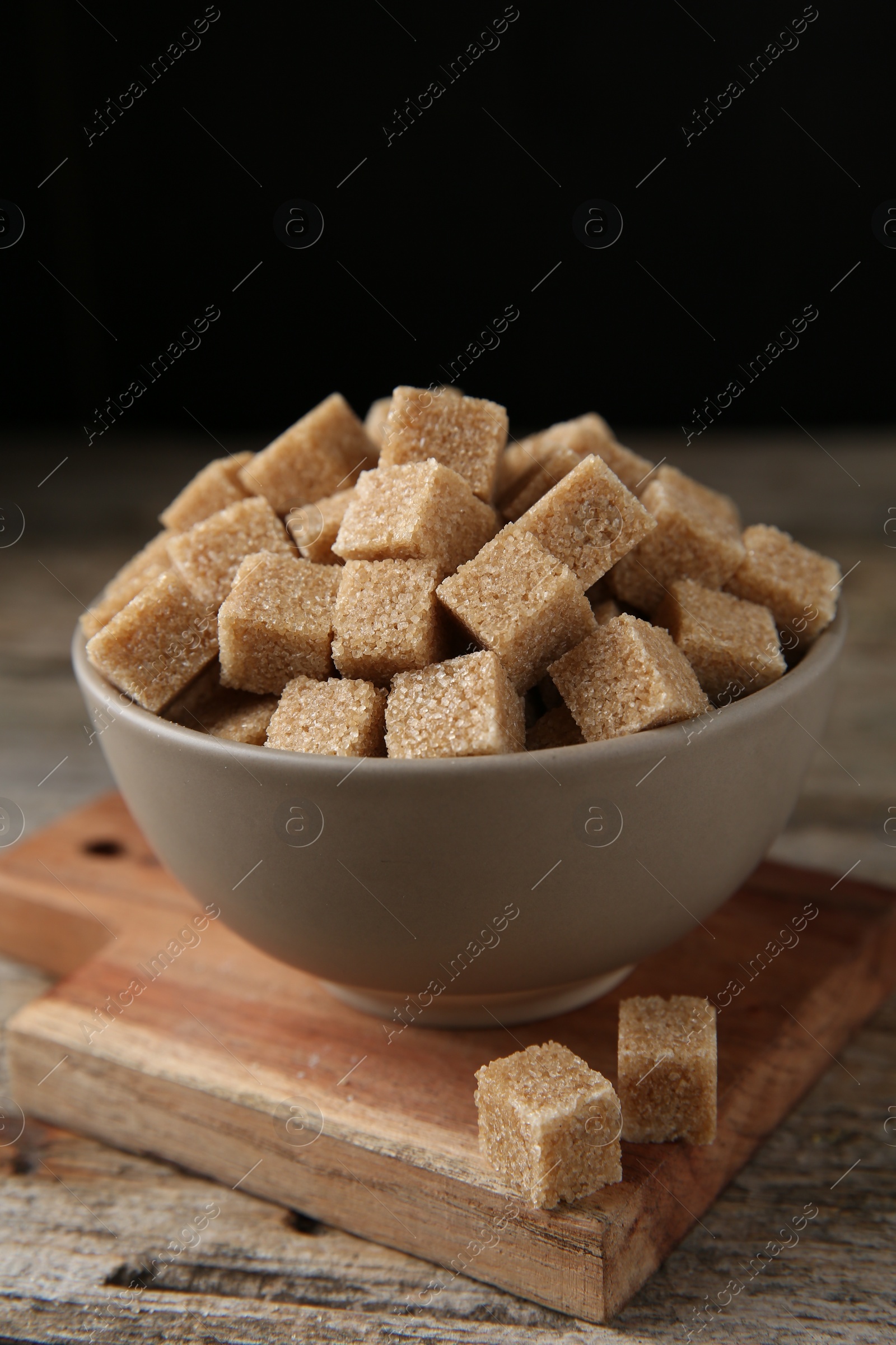 Photo of Brown sugar cubes in bowl on wooden table, closeup