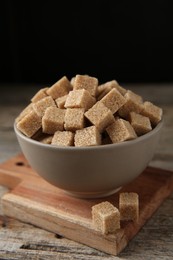 Photo of Brown sugar cubes in bowl on wooden table, closeup