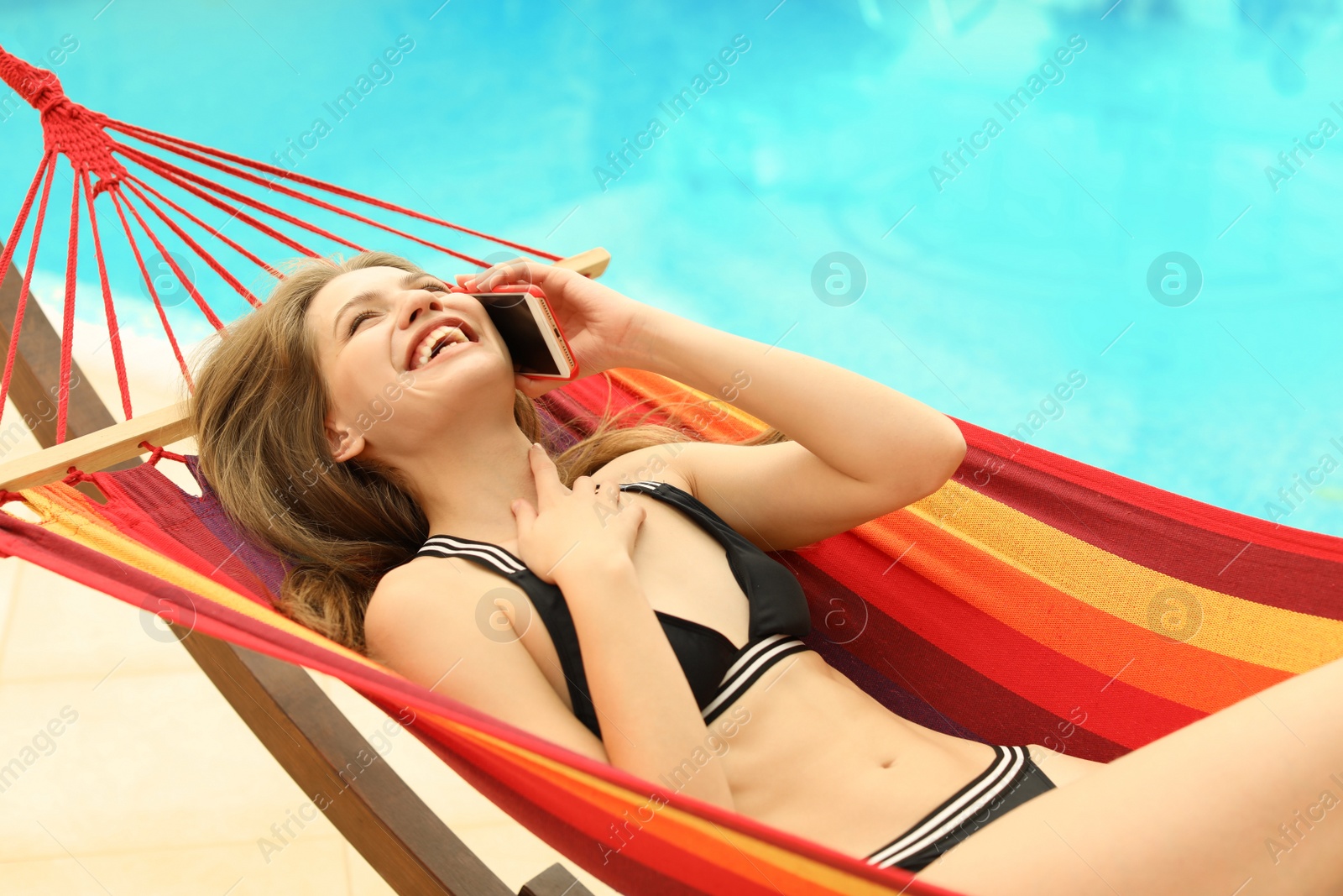 Photo of Young woman talking on phone in hammock near pool