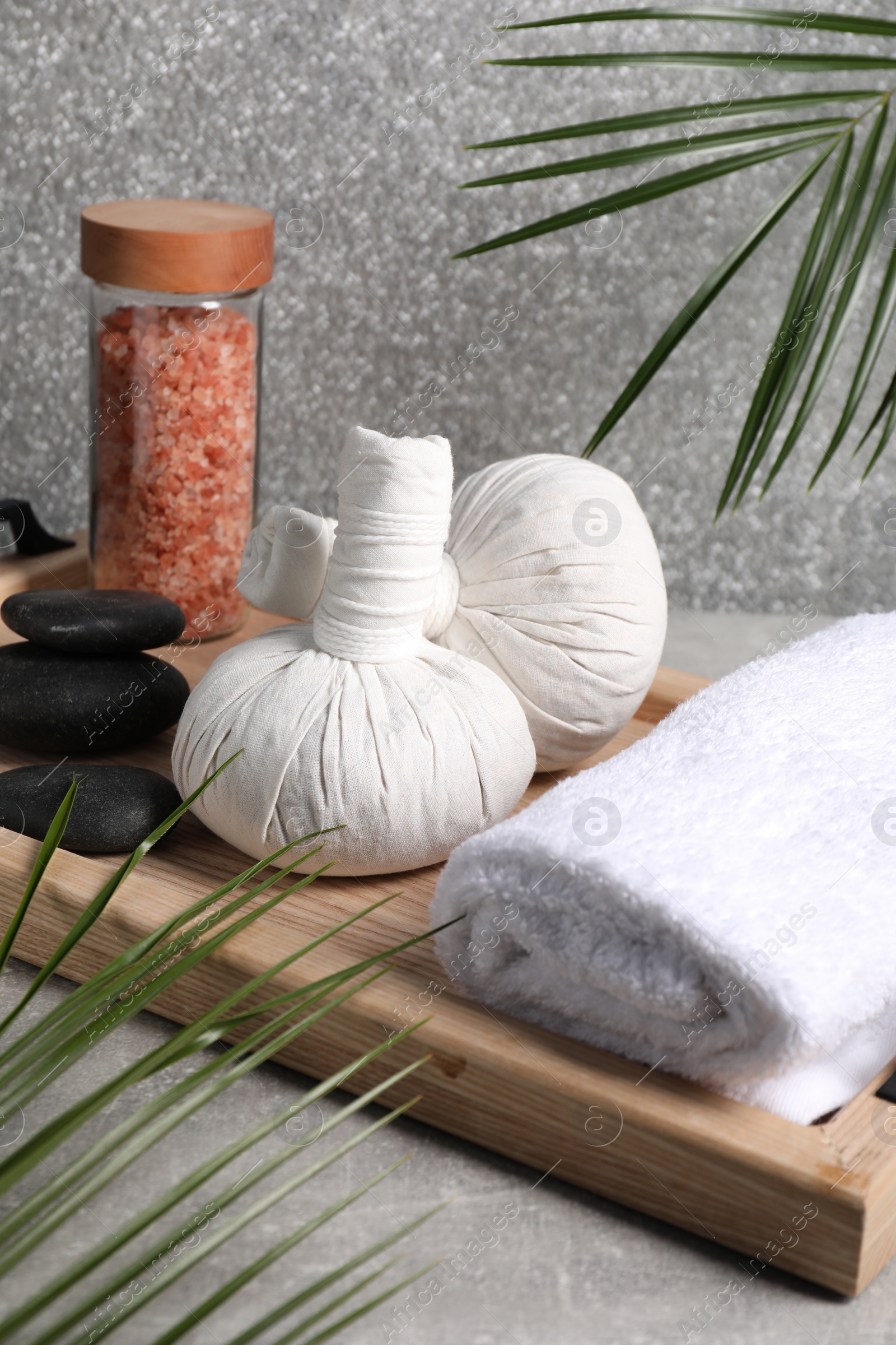 Photo of Herbal massage bags, spa stones, sea salt and rolled towel on grey table