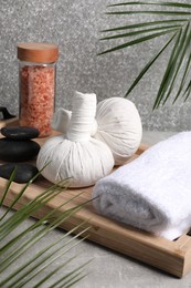 Photo of Herbal massage bags, spa stones, sea salt and rolled towel on grey table
