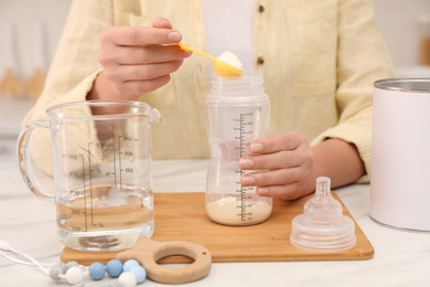 Photo of Woman preparing infant formula at table indoors, closeup. Baby milk