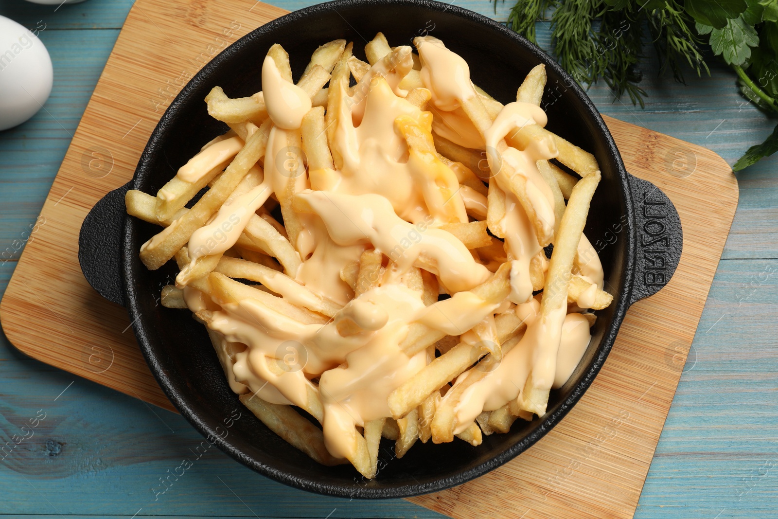 Photo of Delicious french fries with cheese sauce in bowl on light blue wooden table, flat lay