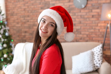 Photo of Beautiful young woman in Santa hat at home. Celebrating Christmas