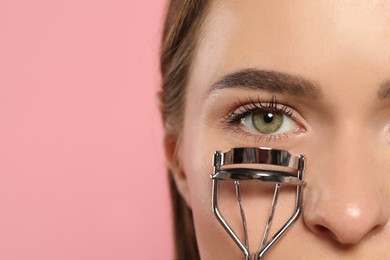 Photo of Woman with eyelash curler on pink background, closeup. Space for text