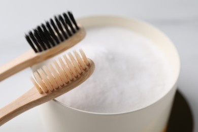 Bamboo toothbrushes and bowl of baking soda on white marble table, closeup