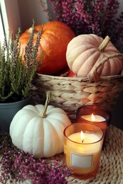 Beautiful heather flowers, burning candles and wicker basket with pumpkins on table