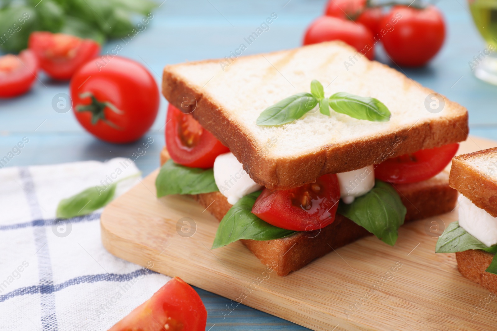 Photo of Delicious Caprese sandwich with mozzarella, tomatoes, basil and pesto sauce on light blue wooden table, closeup. Space for text