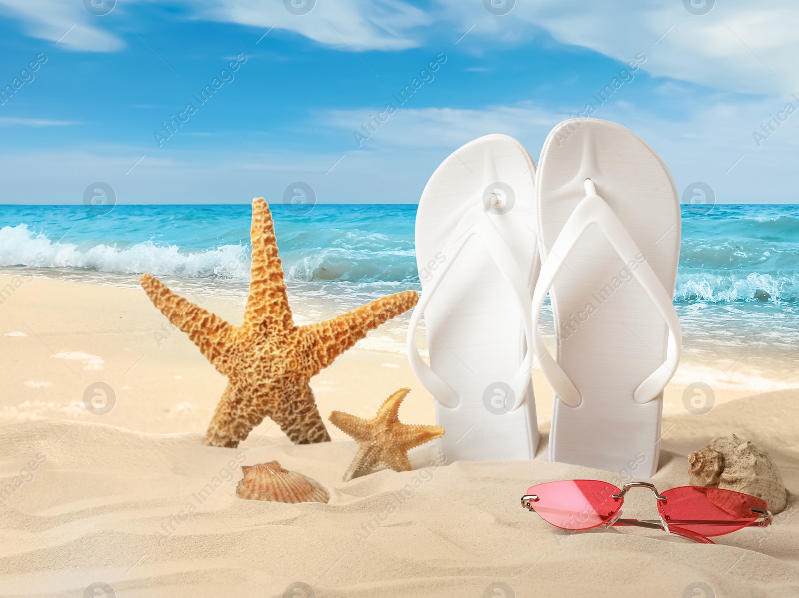 Image of White flip flops, starfishes, sea shells and sunglasses on sandy beach