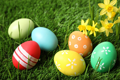 Photo of Colorful Easter eggs and narcissus flowers in green grass