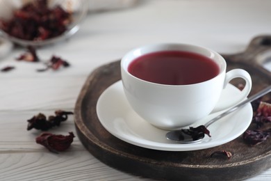 Photo of Delicious hibiscus tea in cup and dry roselle petals on white wooden table, closeup