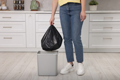 Photo of Woman taking garbage bag out of trash bin in kitchen, closeup