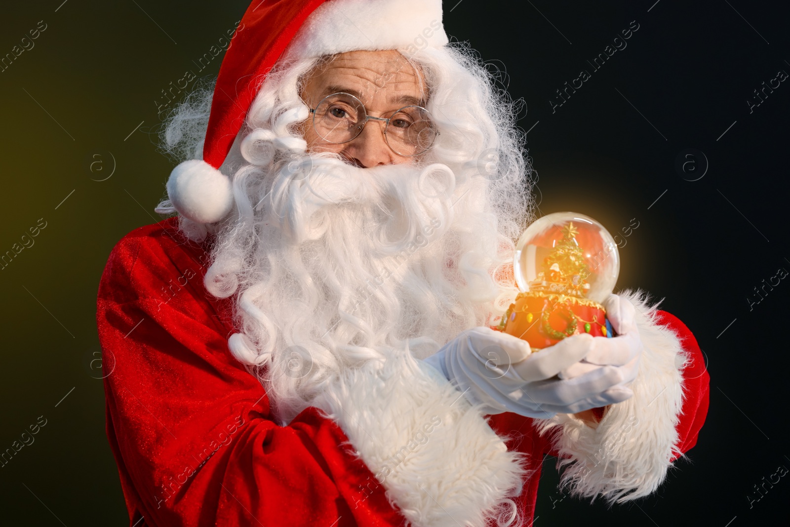 Photo of Merry Christmas. Santa Claus with snow globe on dark background