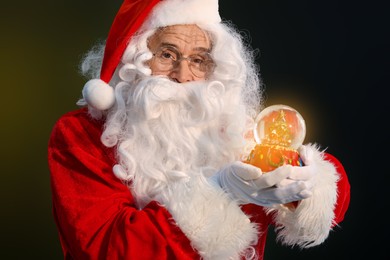 Photo of Merry Christmas. Santa Claus with snow globe on dark background
