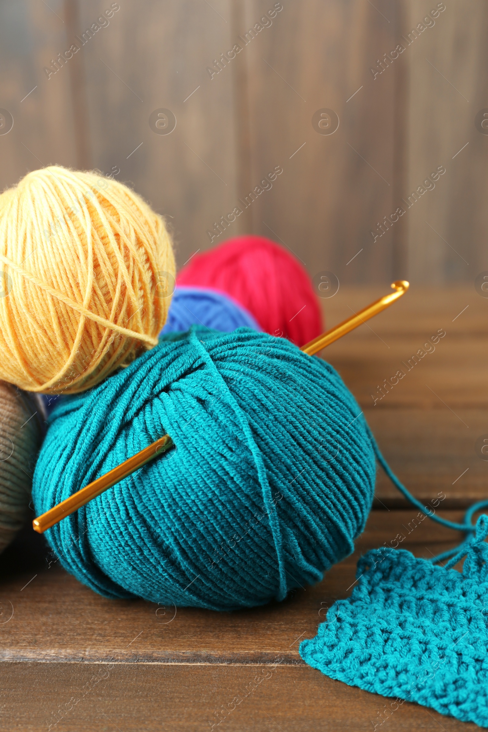 Photo of Clews of colorful knitting threads and crochet hook on wooden table