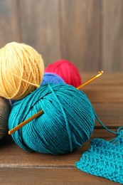 Photo of Clews of colorful knitting threads and crochet hook on wooden table