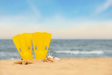 Yellow flippers and seashells on sand outdoors, space for text. Beach objects