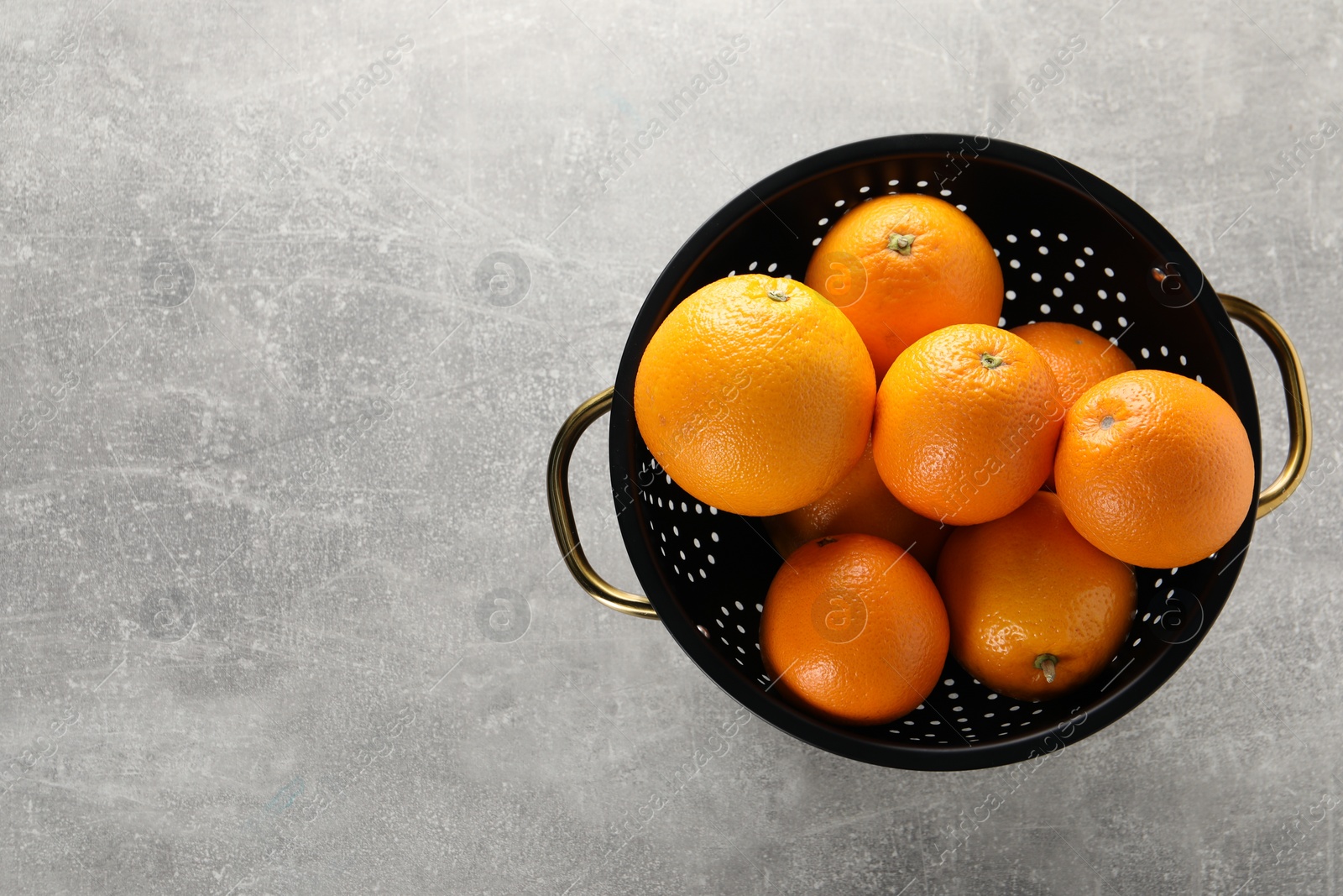 Photo of Fresh ripe oranges in black colander on light grey table, top view. Space for text