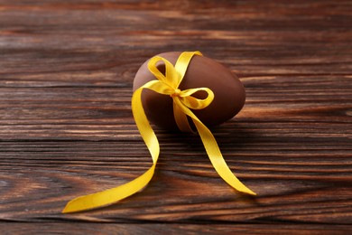 Tasty chocolate egg with yellow bow on wooden table