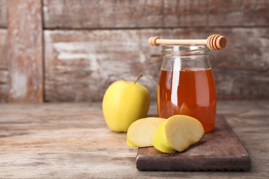 Photo of Jar of honey, apples and dipper on wooden table