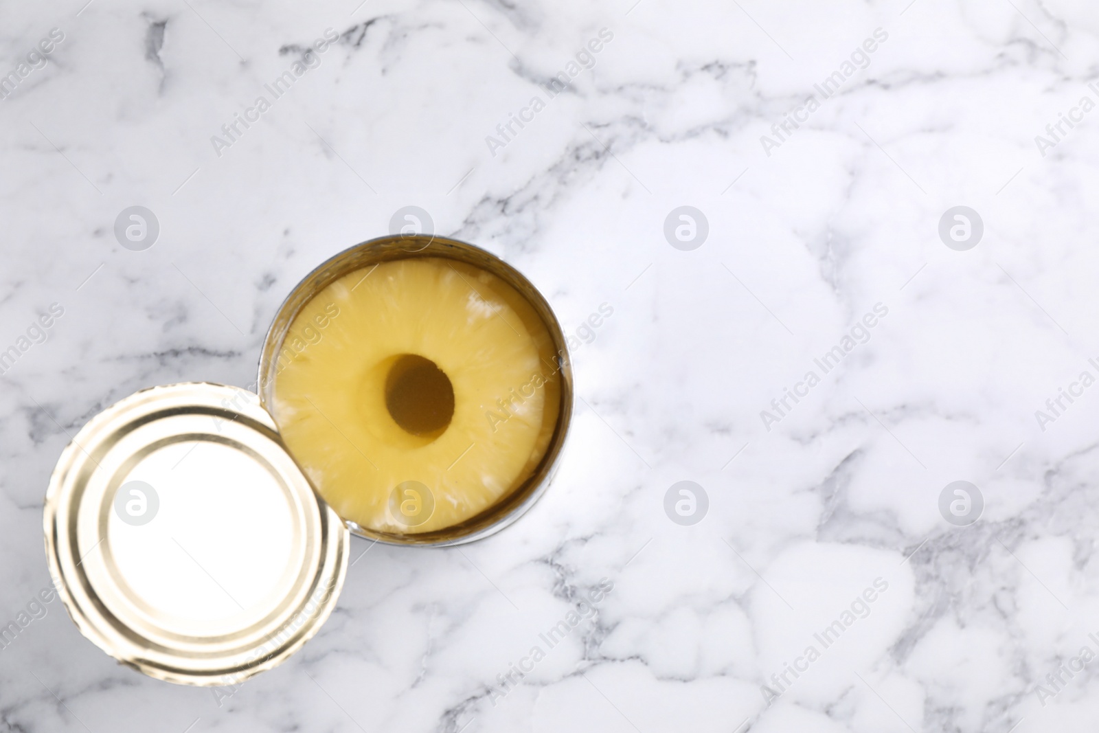 Photo of Tin with canned pineapple on white marble table, top view. Space for text