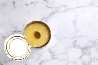 Tin with canned pineapple on white marble table, top view. Space for text