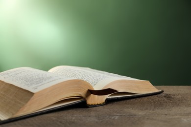 Open Bible on wooden table against green background. Space for text